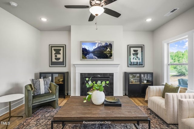 living room with hardwood / wood-style flooring, ceiling fan, and a tile fireplace