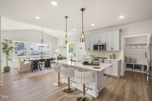 kitchen featuring lofted ceiling, sink, light hardwood / wood-style flooring, decorative light fixtures, and stainless steel appliances