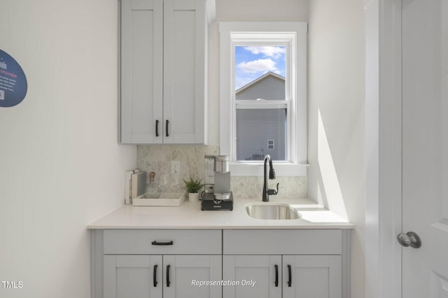 bar with tasteful backsplash, white cabinetry, and sink