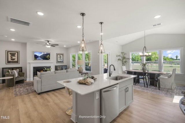 kitchen with sink, stainless steel dishwasher, pendant lighting, a kitchen island with sink, and light wood-type flooring