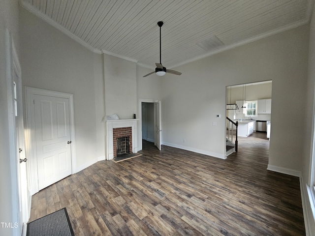 unfurnished living room featuring dark wood-type flooring, crown molding, wooden ceiling, a fireplace, and a high ceiling