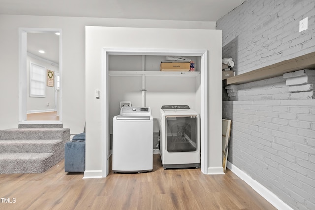 clothes washing area with independent washer and dryer, wood-type flooring, and brick wall