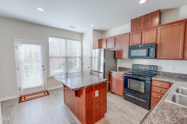 kitchen with a breakfast bar, a center island, black appliances, sink, and light wood-type flooring