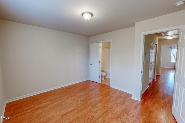 unfurnished bedroom with a closet, a walk in closet, connected bathroom, and light hardwood / wood-style flooring