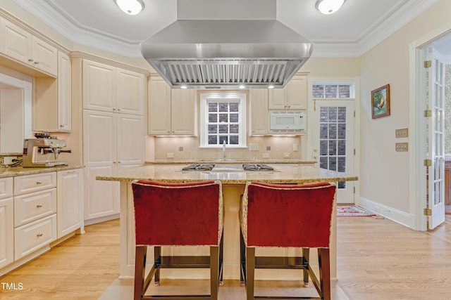 kitchen with white microwave, ornamental molding, range hood, and light wood-type flooring