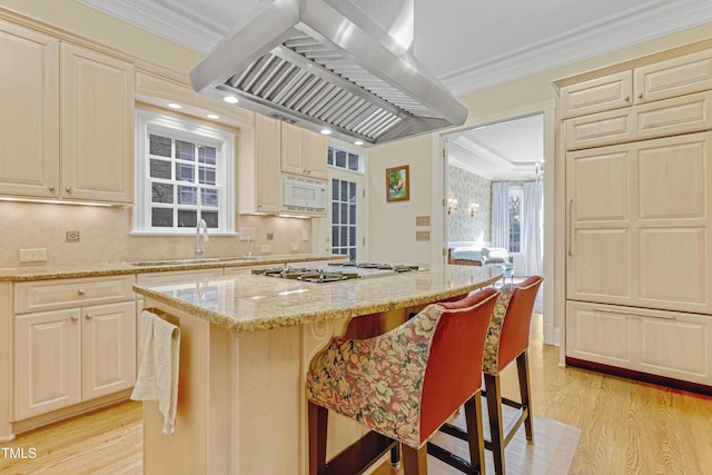 kitchen with a kitchen bar, light stone counters, ornamental molding, island range hood, and a center island