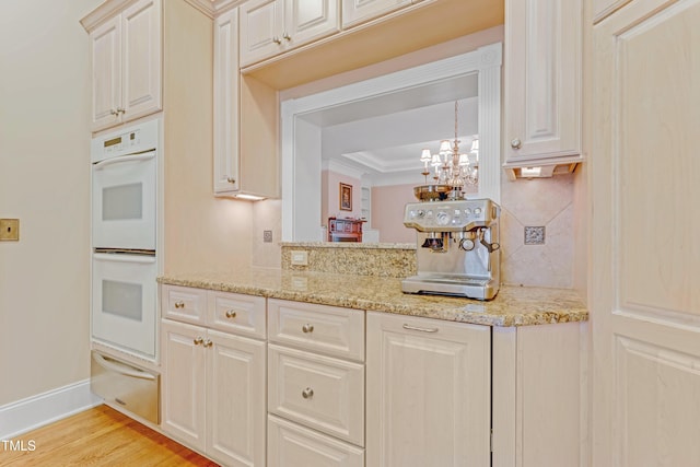 kitchen with decorative backsplash, light hardwood / wood-style floors, light stone counters, and double oven