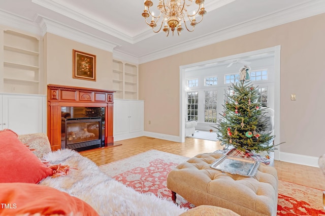 living room featuring ornamental molding, light hardwood / wood-style floors, built in shelves, a fireplace, and a chandelier