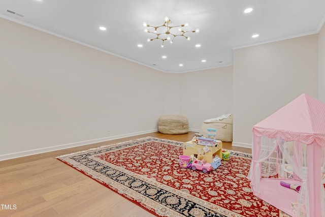 recreation room featuring hardwood / wood-style floors, a notable chandelier, and ornamental molding