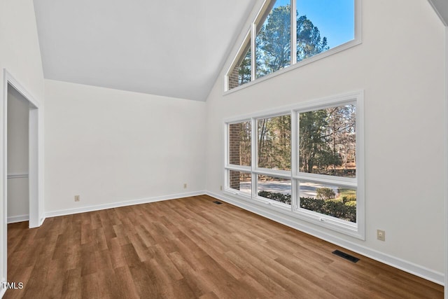 unfurnished room with high vaulted ceiling, baseboards, visible vents, and wood finished floors