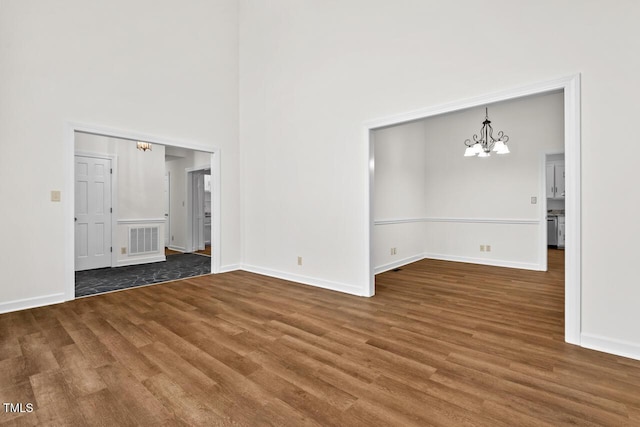 unfurnished living room featuring baseboards, visible vents, a towering ceiling, wood finished floors, and an inviting chandelier