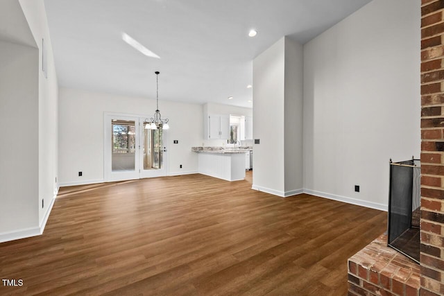 unfurnished living room with baseboards, dark wood-style floors, an inviting chandelier, a sink, and recessed lighting