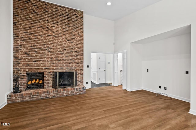 unfurnished living room featuring recessed lighting, a brick fireplace, baseboards, and wood finished floors