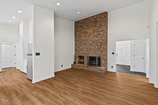 unfurnished living room featuring a towering ceiling, a brick fireplace, baseboards, and wood finished floors