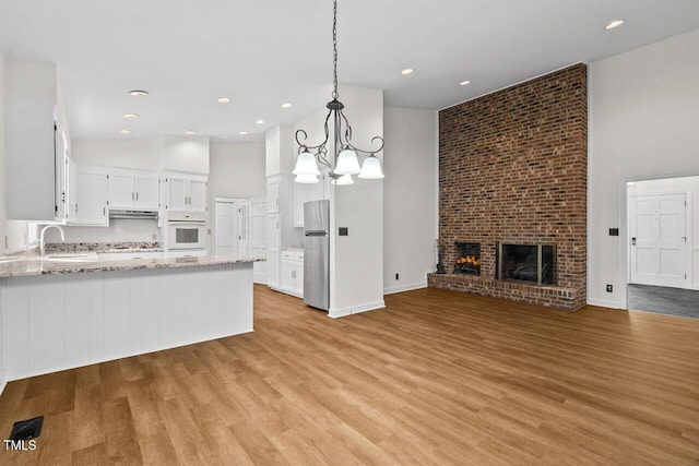 kitchen with white oven, freestanding refrigerator, a brick fireplace, open floor plan, and a sink