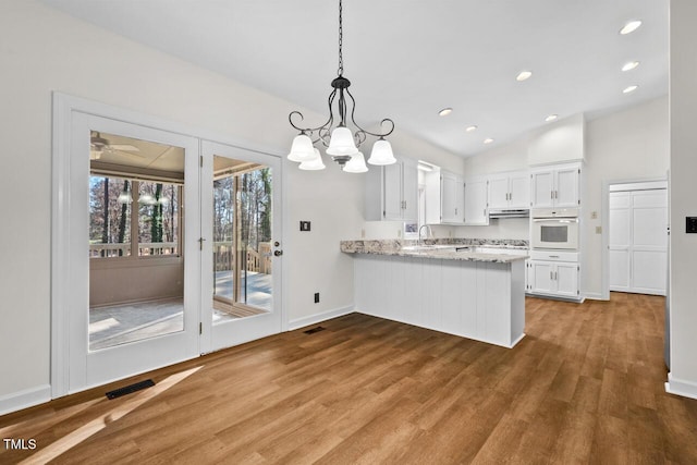 kitchen with white oven, visible vents, a peninsula, wood finished floors, and under cabinet range hood