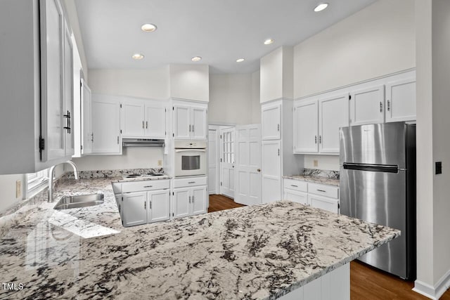 kitchen featuring white appliances, white cabinets, a peninsula, light stone countertops, and a sink