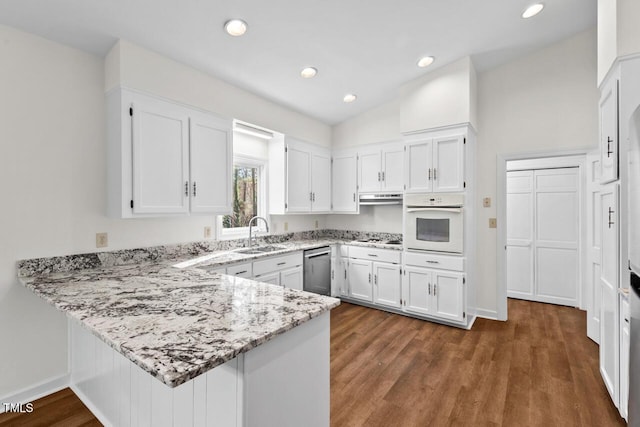 kitchen with light stone counters, white oven, white cabinetry, a sink, and a peninsula