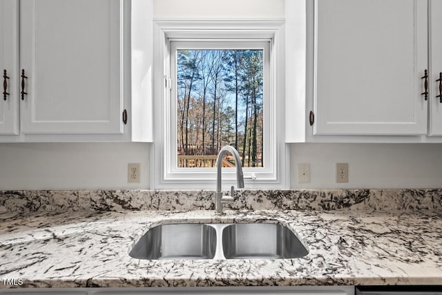 kitchen featuring light stone counters, a sink, and white cabinetry