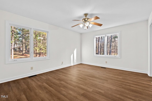 spare room with dark wood-style flooring, visible vents, and baseboards