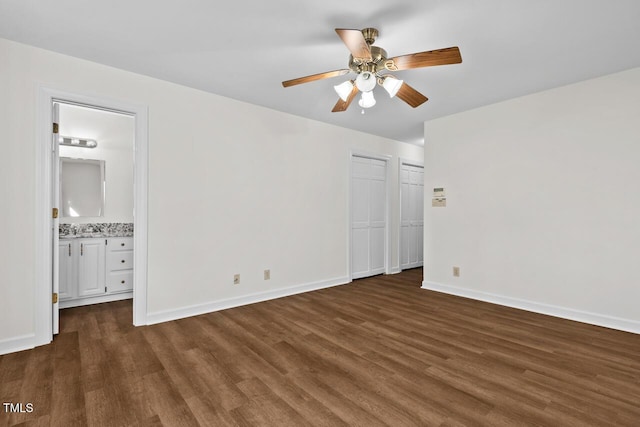 unfurnished bedroom with ensuite bathroom, dark wood-type flooring, and baseboards