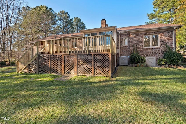 back of house featuring brick siding, a chimney, a lawn, a deck, and cooling unit