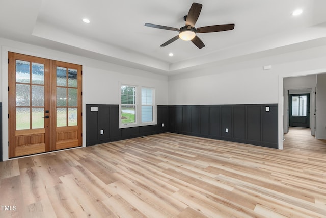 spare room featuring a tray ceiling, ceiling fan, french doors, and light wood-type flooring