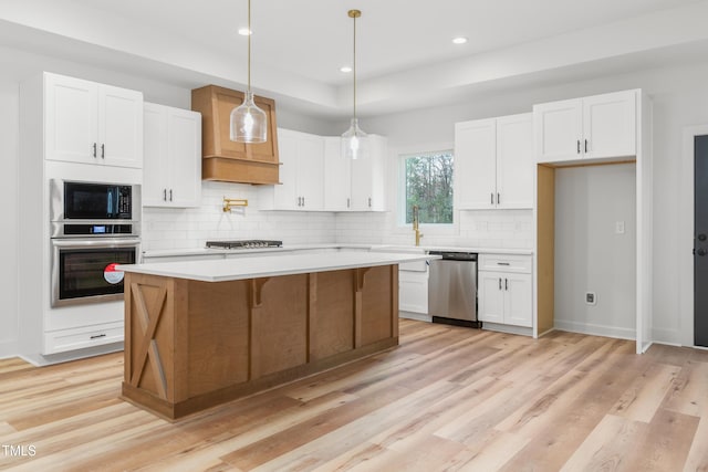 kitchen with pendant lighting, light hardwood / wood-style flooring, appliances with stainless steel finishes, a kitchen island, and white cabinetry