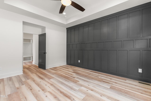 unfurnished bedroom featuring ceiling fan, light wood-type flooring, a tray ceiling, and a closet