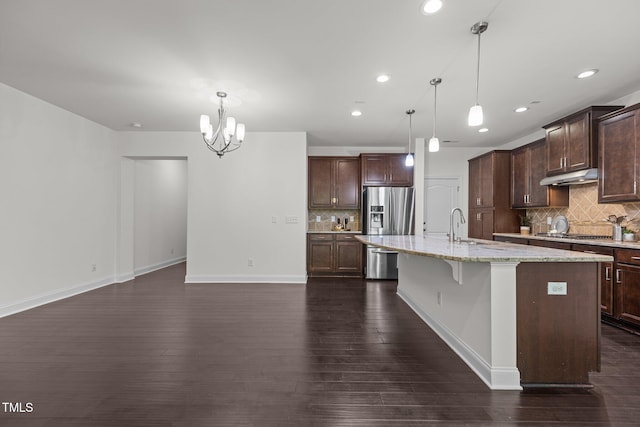 kitchen featuring a center island with sink, dark hardwood / wood-style floors, dark brown cabinets, light stone counters, and a breakfast bar area