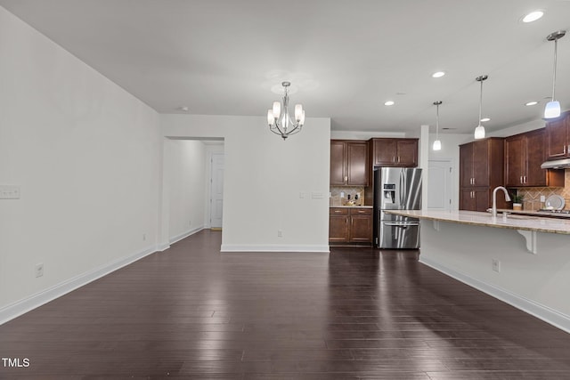 interior space with a kitchen bar, tasteful backsplash, stainless steel fridge with ice dispenser, dark hardwood / wood-style floors, and hanging light fixtures