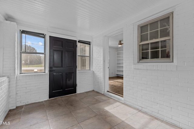 tiled entrance foyer with wood ceiling, ceiling fan, crown molding, and brick wall