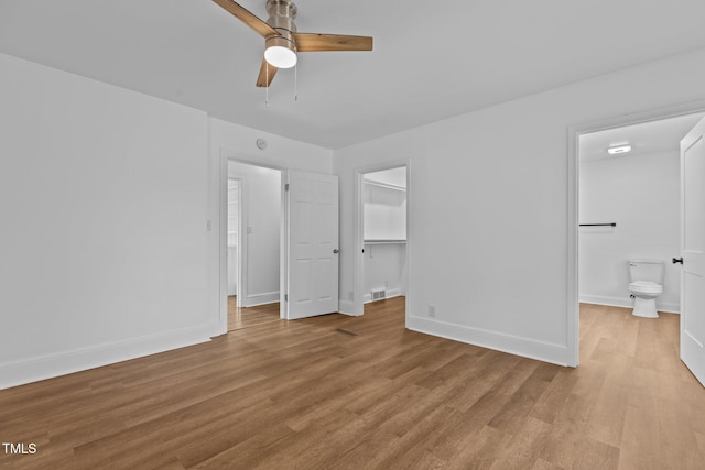 unfurnished bedroom featuring connected bathroom, a walk in closet, ceiling fan, and light wood-type flooring