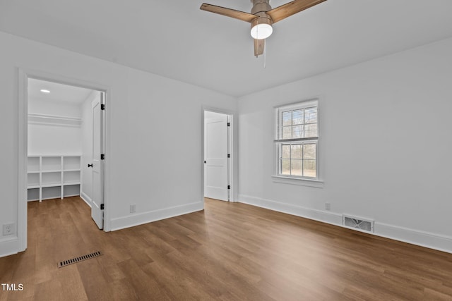 unfurnished bedroom with a walk in closet, ceiling fan, a closet, and hardwood / wood-style flooring