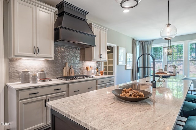 kitchen with backsplash, custom exhaust hood, stainless steel gas cooktop, sink, and pendant lighting