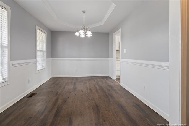 unfurnished dining area featuring ornamental molding, a tray ceiling, dark wood-type flooring, and a notable chandelier