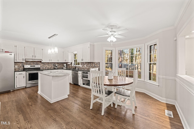 kitchen featuring decorative light fixtures, backsplash, stainless steel appliances, and white cabinetry