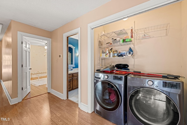 clothes washing area featuring a textured ceiling, ceiling fan, washer and clothes dryer, and light hardwood / wood-style flooring