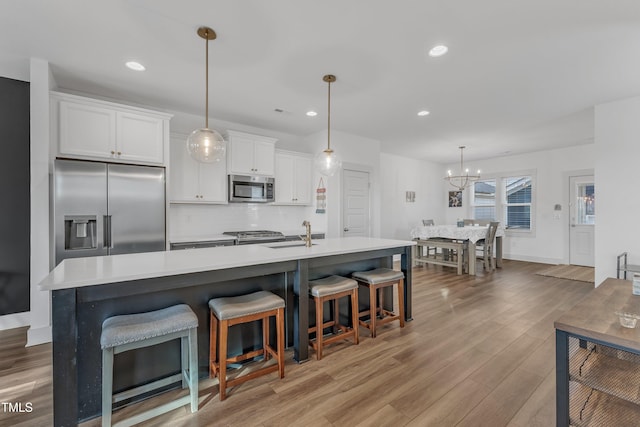 kitchen featuring white cabinetry, a center island with sink, stainless steel appliances, and light wood-type flooring