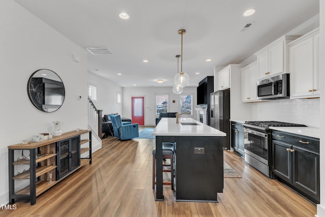 kitchen featuring white cabinetry, hanging light fixtures, stainless steel appliances, light hardwood / wood-style flooring, and an island with sink