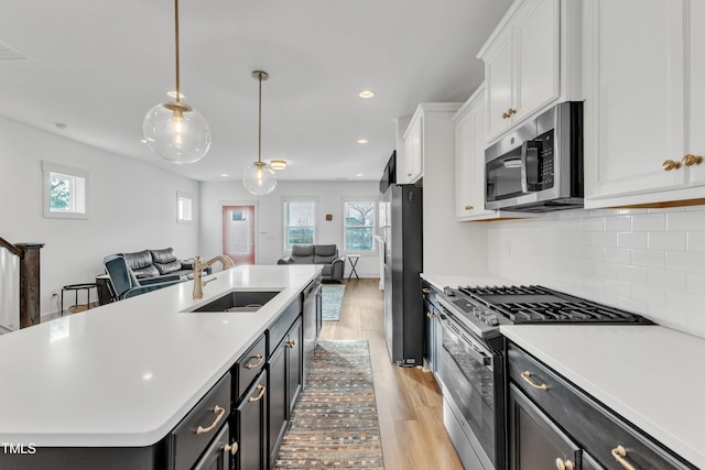 kitchen featuring stainless steel appliances, a wealth of natural light, a center island with sink, and sink