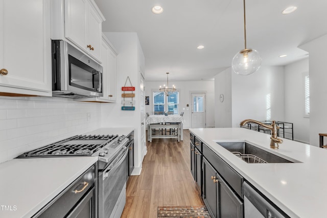 kitchen with sink, white cabinetry, stainless steel appliances, and hanging light fixtures