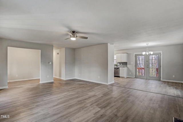 unfurnished living room with ceiling fan with notable chandelier, light wood-type flooring, and french doors