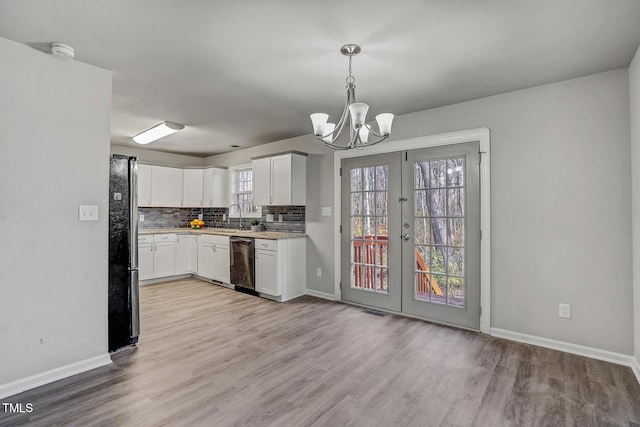 kitchen featuring light wood-type flooring, black fridge, stainless steel dishwasher, decorative light fixtures, and white cabinetry