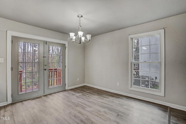 unfurnished dining area featuring french doors, an inviting chandelier, and hardwood / wood-style flooring