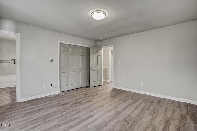 unfurnished bedroom with ensuite bathroom, light hardwood / wood-style floors, and a closet