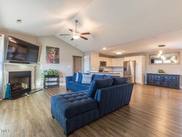 living room with ceiling fan with notable chandelier, light hardwood / wood-style floors, and lofted ceiling