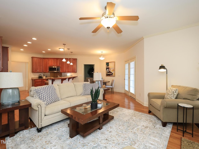 living room with ceiling fan, crown molding, and light wood-type flooring