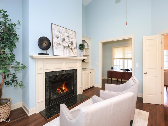 living room with a towering ceiling, dark hardwood / wood-style floors, and a premium fireplace