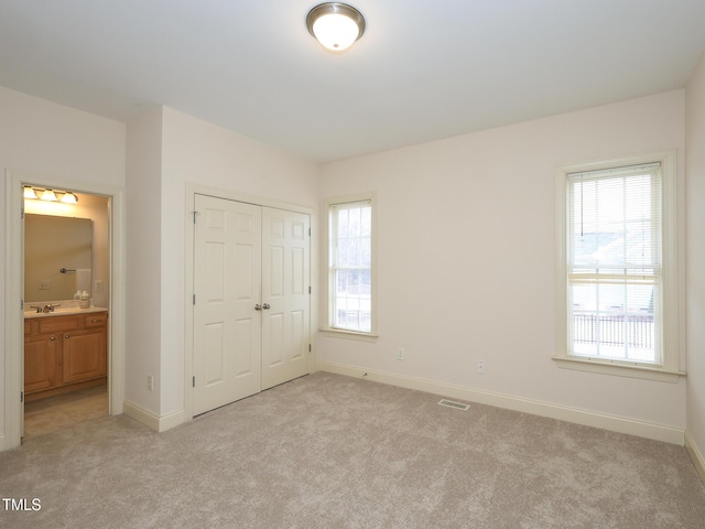 unfurnished bedroom featuring light carpet, ensuite bathroom, a closet, and sink